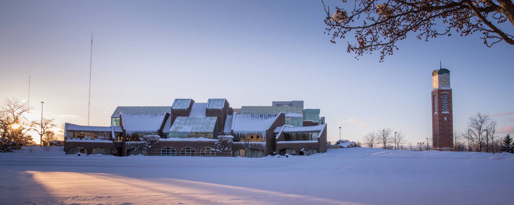 photograph of the outside of the student services building, Kirkhof, on allendale campus at wintertime. there is snow on the ground and on the building. there is a hint of sunlight peaking over the building